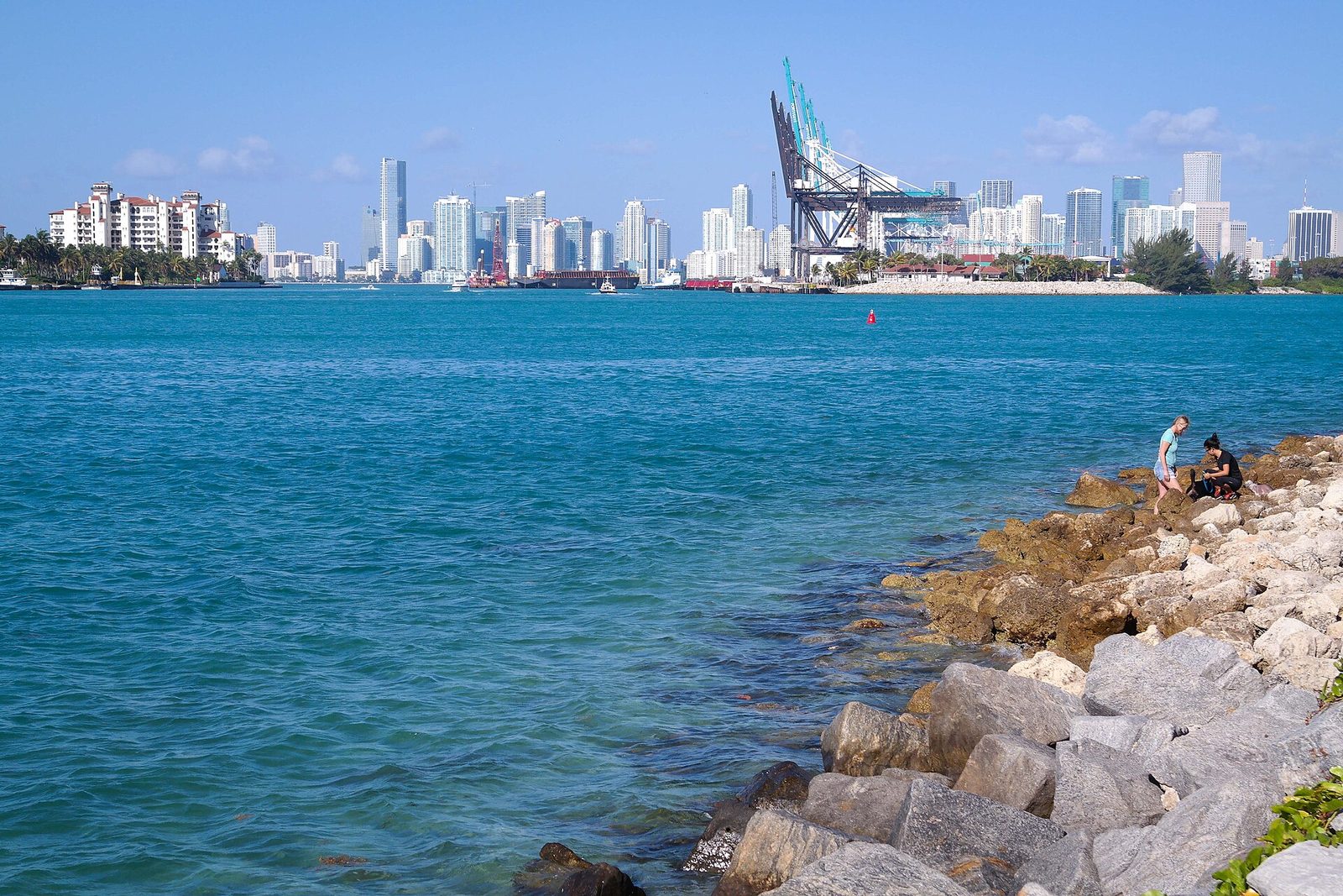 The downtown Miami skyline across turquoise bay water, seen from the shoreline of South Pointe Park in Miami Beach