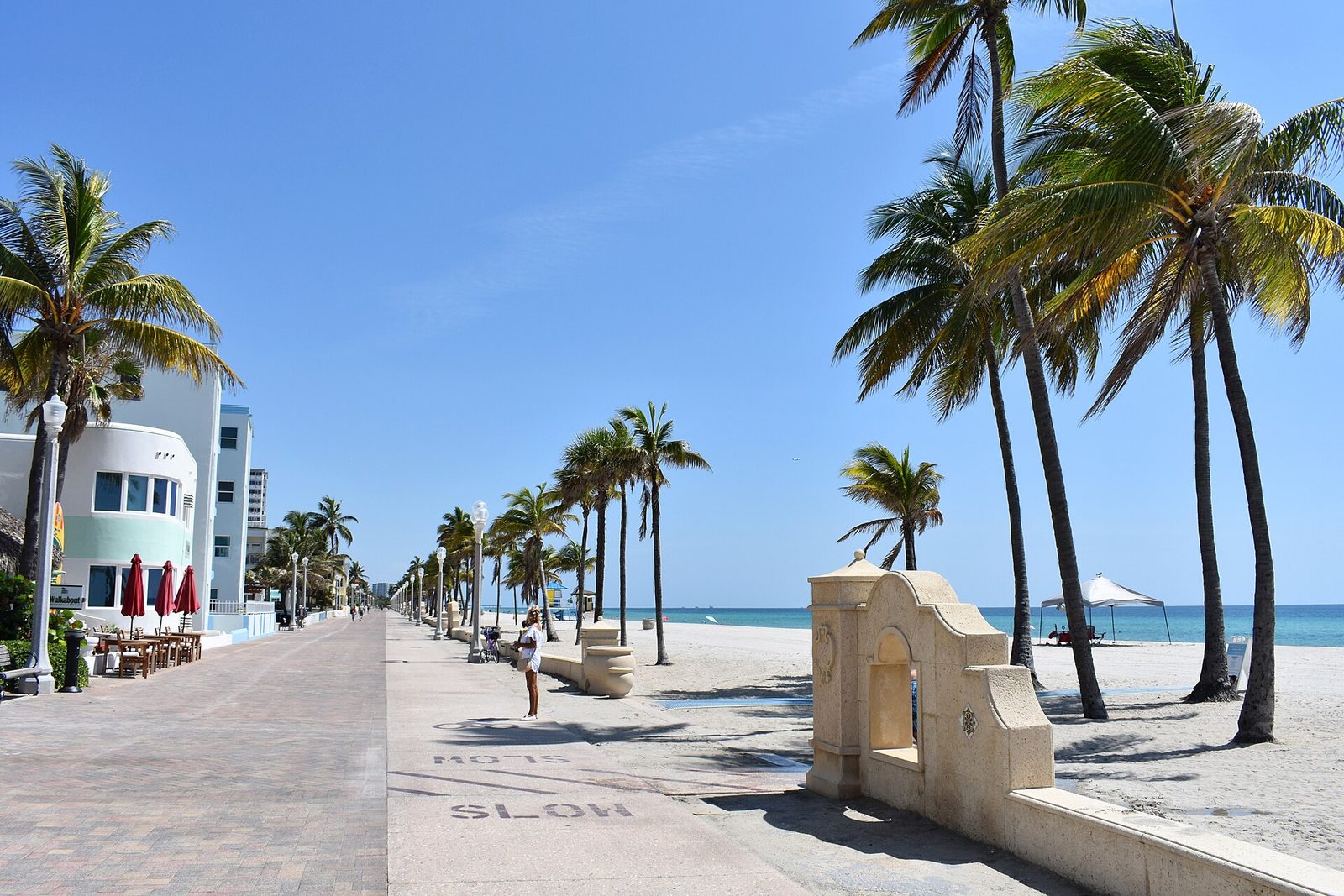 The palm-lined Hollywood Beach Broadwalk on a sunny day, with the brick promenade, beach, and Atlantic Ocean in Hollywood, Florida