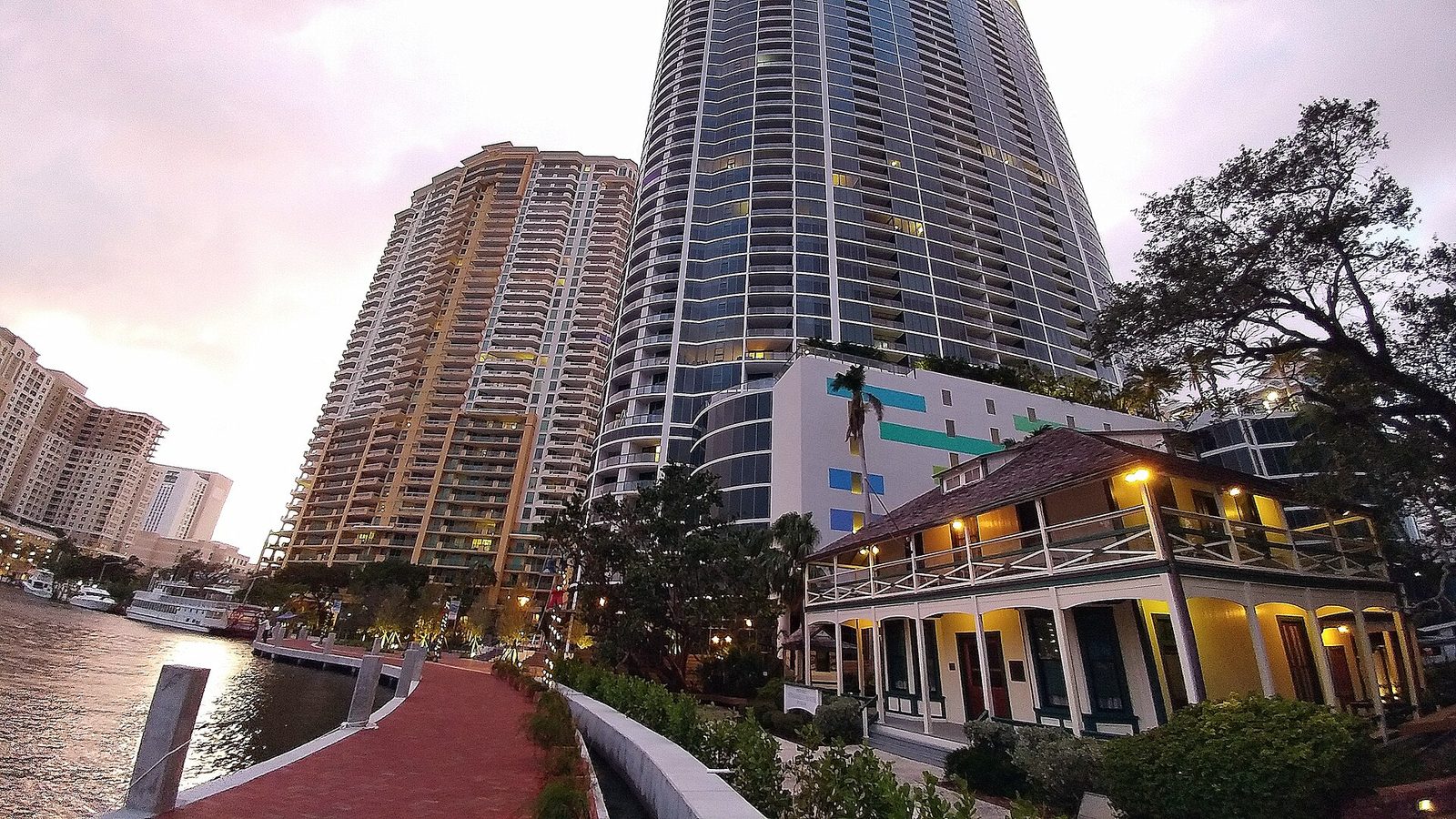 The Riverwalk promenade along the New River at dusk in downtown Fort Lauderdale, with the historic Stranahan House lit up and city towers behind it