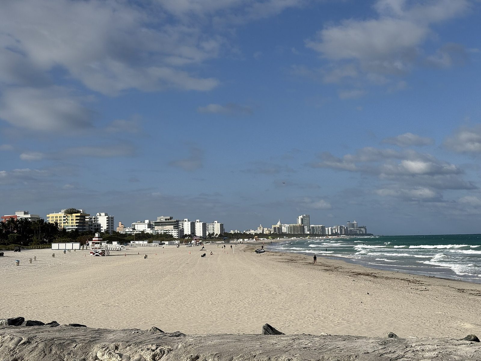 Miami Beach's shoreline looking north from South Pointe Park, with a lifeguard stand on the sand and the beach skyline in the distance