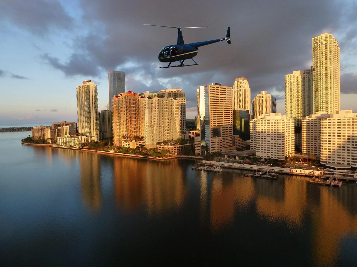 A black helicopter flying over Miami's waterfront at golden hour