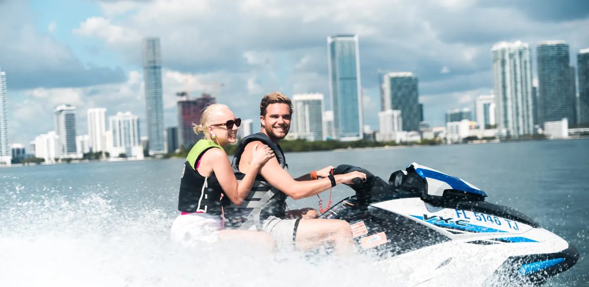 A couple riding a jet ski together on Biscayne Bay with the Miami skyline behind