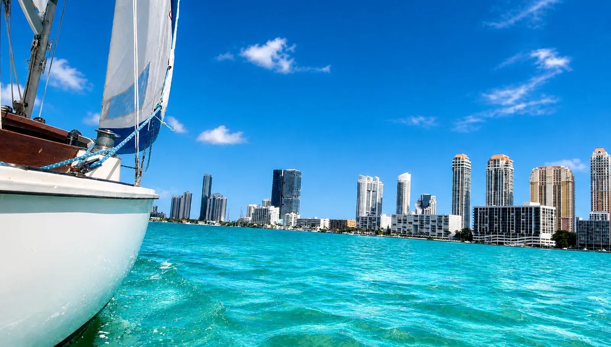 A small sailboat on the turquoise water of Biscayne Bay with the Miami skyline behind